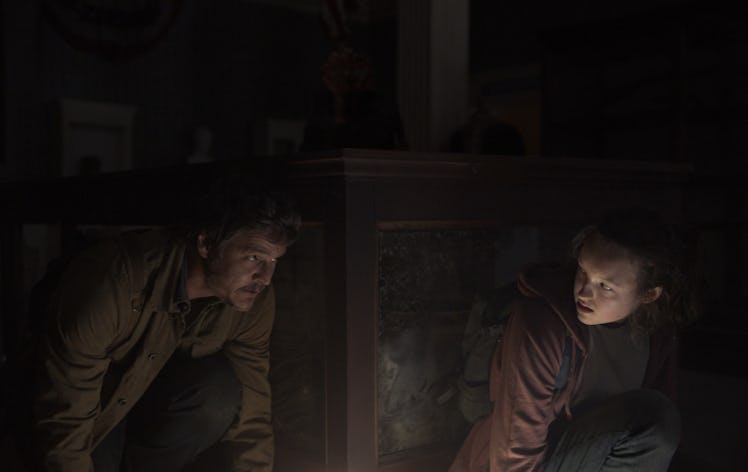 Joel (Pedro Pascal) and Ellie (Bella Ramsey) crouch behind a museum display case in The Last of Us E...