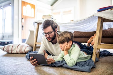 Father and son watching iPad together while laying on the floor. 