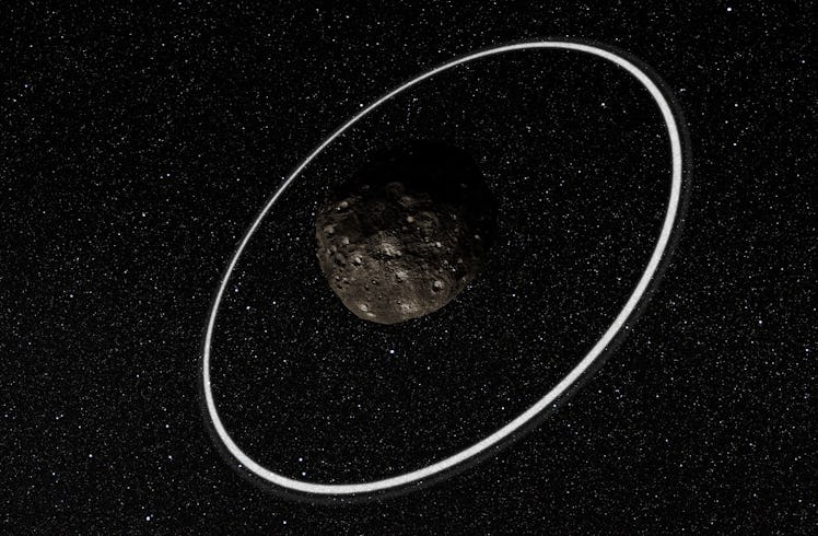 color image of a rocky asteroid encircled by thin white rings