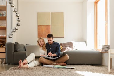 Couple sitting on floor looking at paperwork and laptop