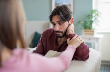 Man looking distraught as woman reaches out for his arm.
