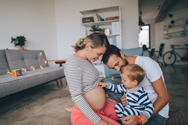 A dad and pregnant mom sit with their baby, who reaches out to his mom's belly.