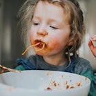 A child eating a bowl of spaghetti, getting it all over her face.