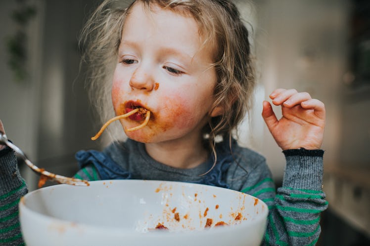 A child eating a bowl of spaghetti, getting it all over her face.