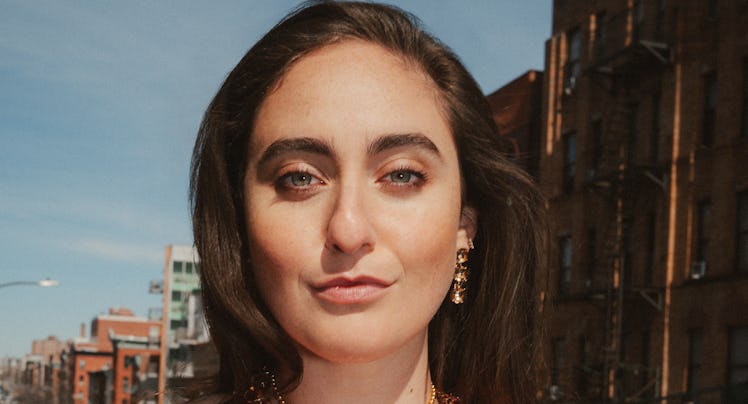 Catherine Cohen, a comedian, stares into the camera with a bemused expression. She's wearing a black...