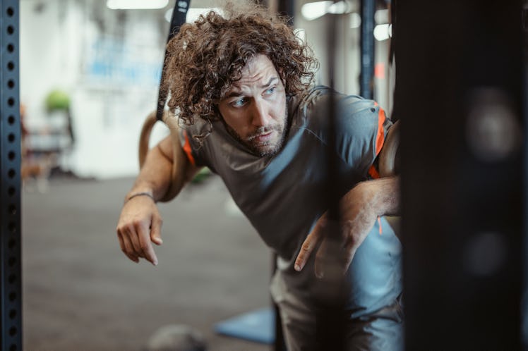 A sweaty man resting on gymnastics rings at the gym.