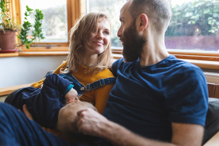 A happy wife and husband sit on the couch with their baby.