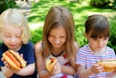 三个孩子在外面吃热狗。