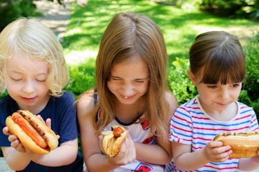 Three kids eating hot dogs outside.