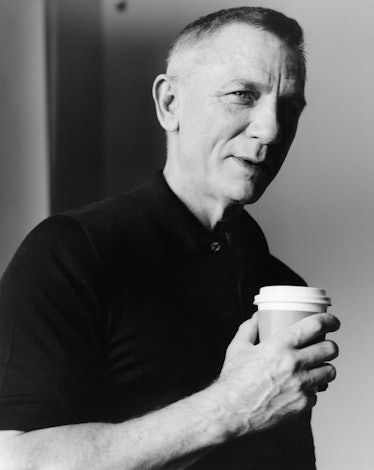 Daniel Craig holds a cup of coffee and wears a black polo shirt.