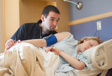 A man comforts his pregnant wife, who is in a hospital bed.