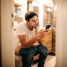 A man sitting on the toilet with his pants down while on his phone.