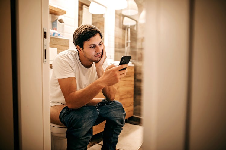 A man sitting on the toilet with his pants down while on his phone.