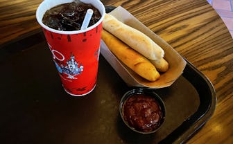 Breadsticks, a thing of marinara sauce, and a cup of coke on a table.