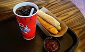 Breadsticks, a thing of marinara sauce, and a cup of coke on a table.