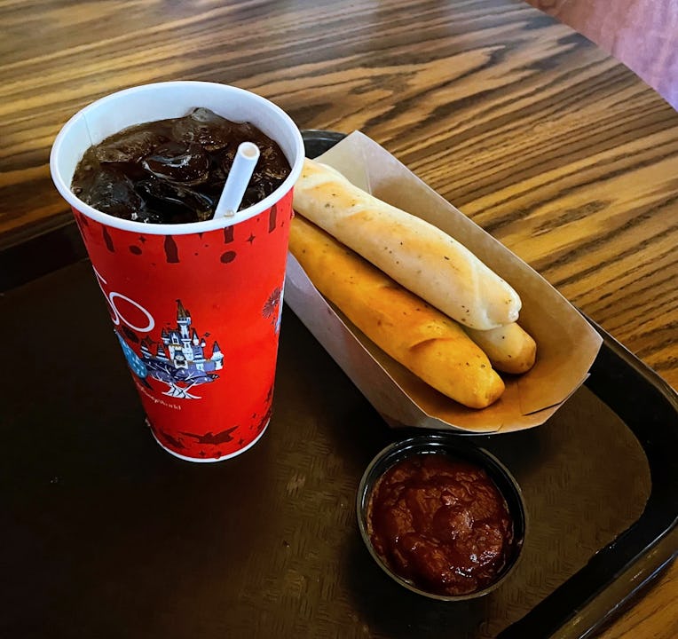 Breadsticks, a thing of marinara sauce, and a cup of coke on a table.