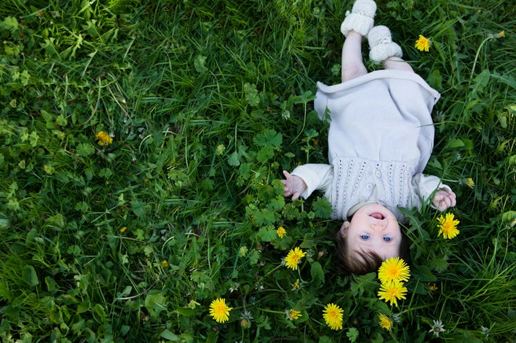 A baby lying in grass with dandelions.