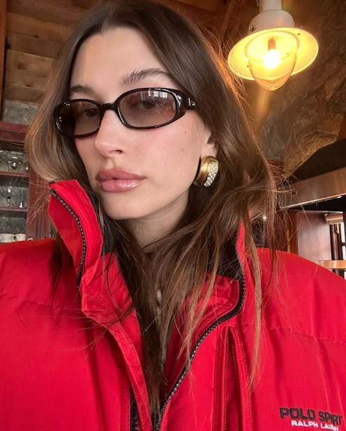 hailey bieber wearing a red coat, sunglasses, and gold earrings
