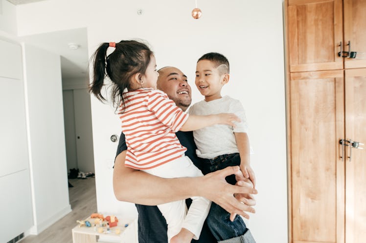 A dad holding his two kids in his arms and smiling.