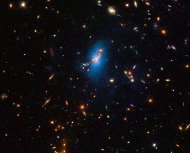 color photo of blackness dotted with tiny galaxies, one group of which is surrounded by blue haze