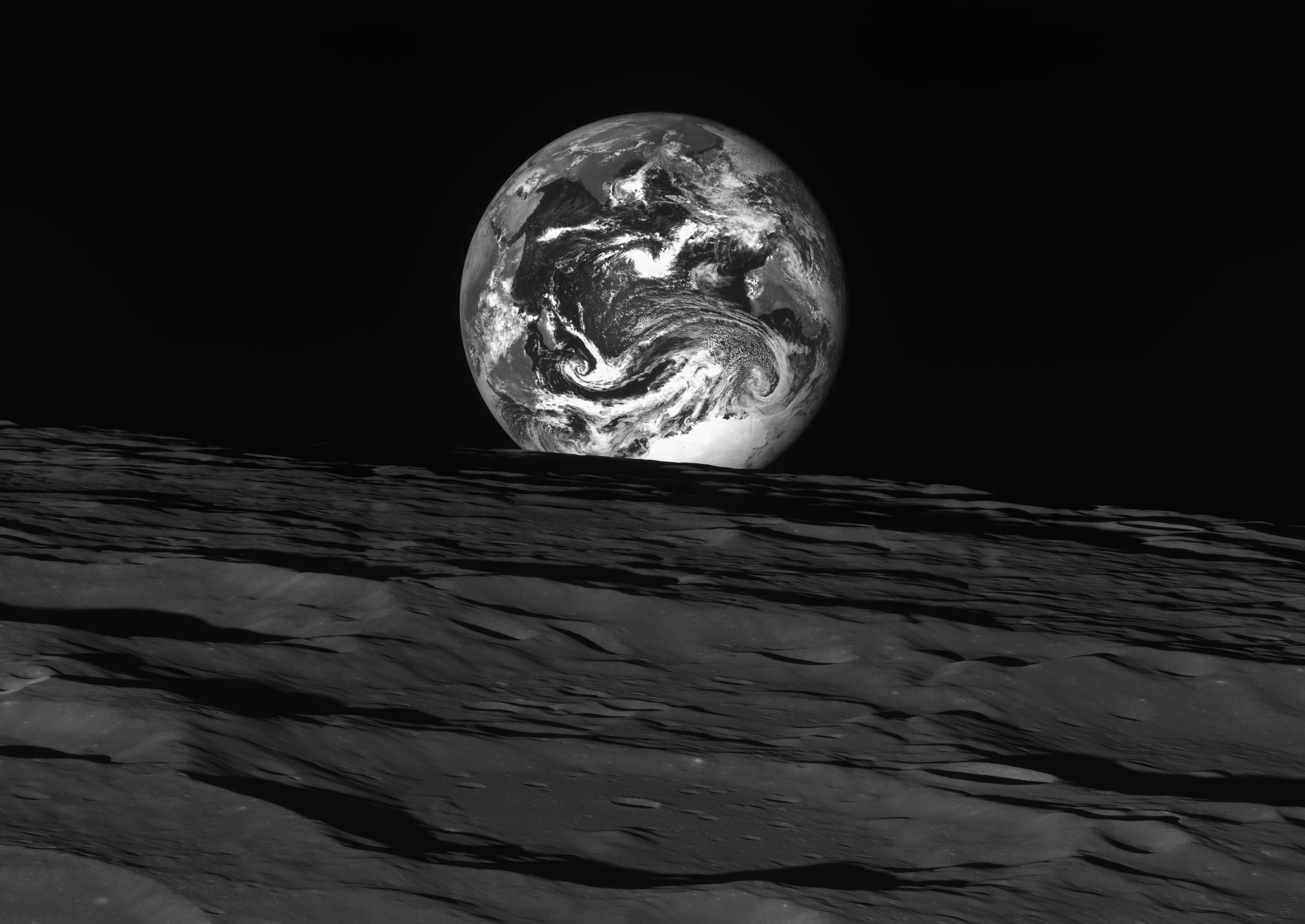 The Earth, appearing as a black and white marble with streaks of clouds across its atmosphere, peeks...