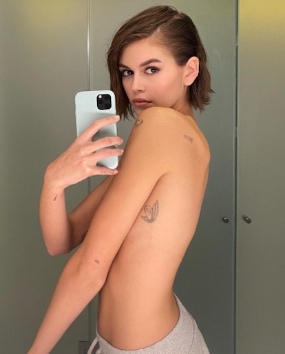 Kaia Gerber small tattoos on ribs in shirtless mirror selfie with baby blue iphone case and side-par...