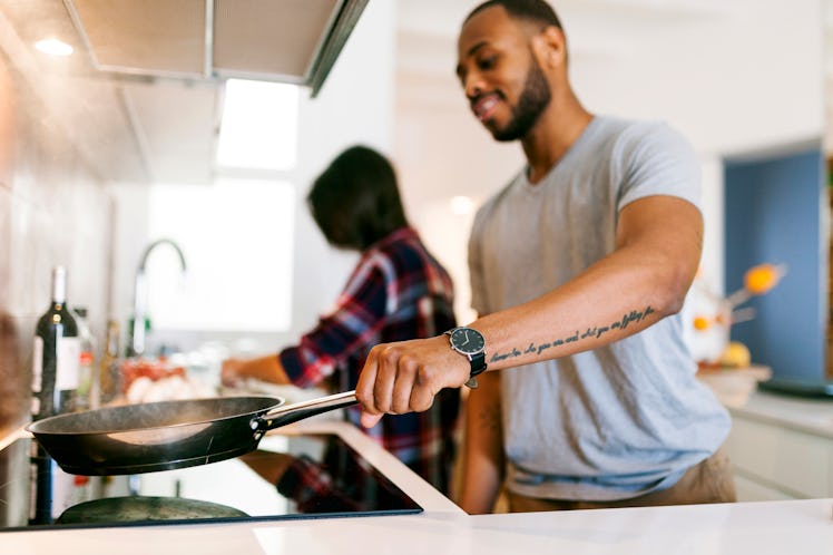 A man cooking in a pan in the kitchen with his wife.
