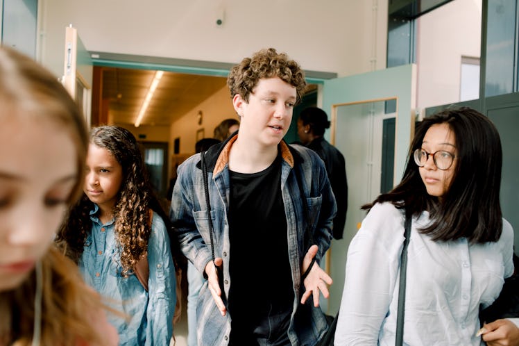 A boy walks through a school hallway with two girls.