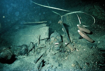 Color photograph of a skull lying between joists of a shipwreck, all with a greenish-bluish tint.