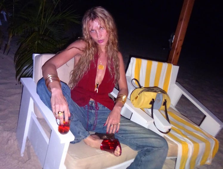Bella Hadid wearing jeans and a red top sitting on a beach chair