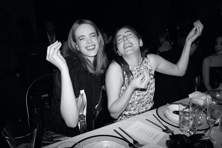 Stacy Martin and Alana Haim cheesing for the camera at the dinner table