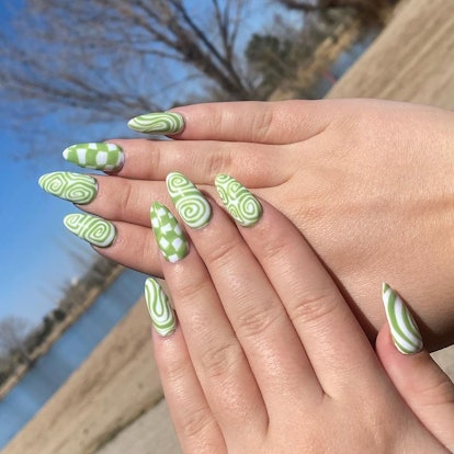 Um design moderno de nail art verde e branco para 2023 que combina unhas xadrez e nail art em espiral.