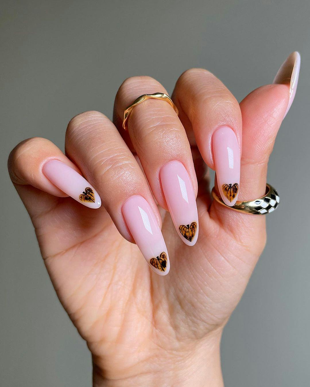 Tiny heart-shaped pumpkins on nude nails are a cute pumpkin nail art design idea for fall 2023.
