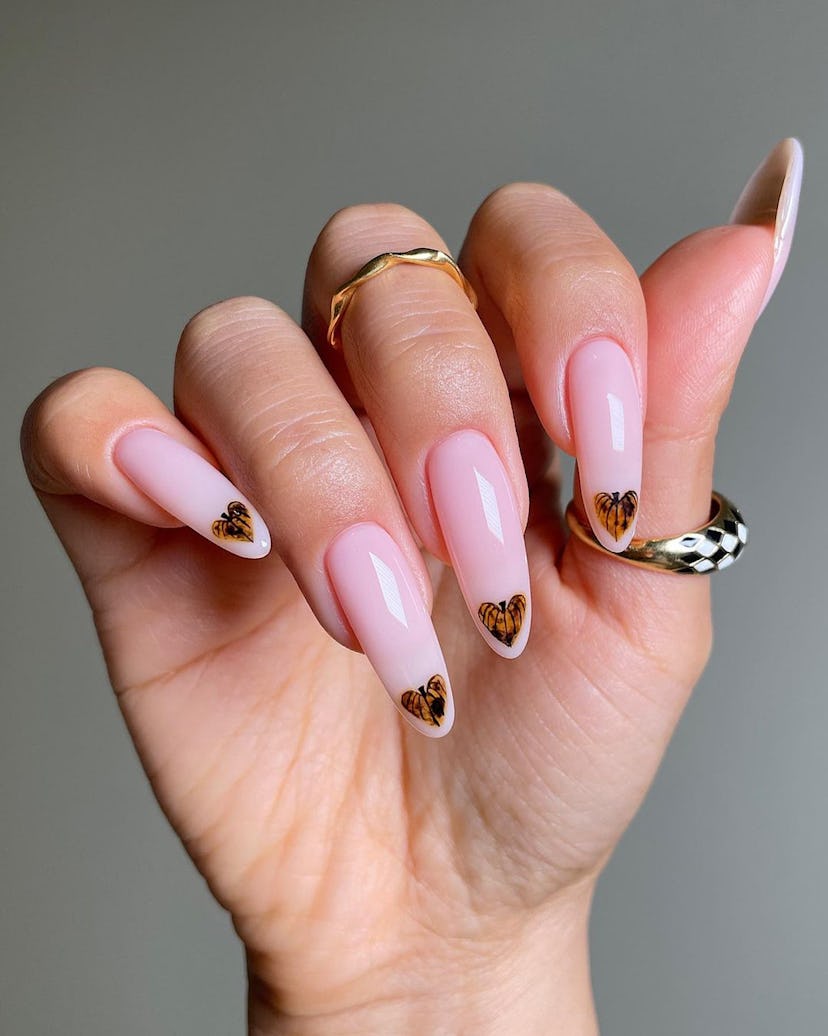 Tiny heart-shaped pumpkins on nude nails are a cute pumpkin nail art design idea for fall 2023.