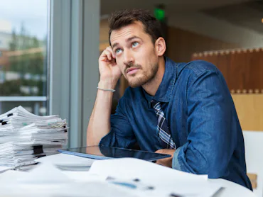 Man sitting at desk looking up into the ceiling and thinking