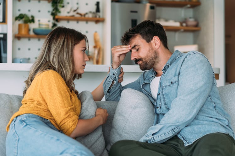 Man and woman sit on a couch frustrated with one another as man rubs forehead