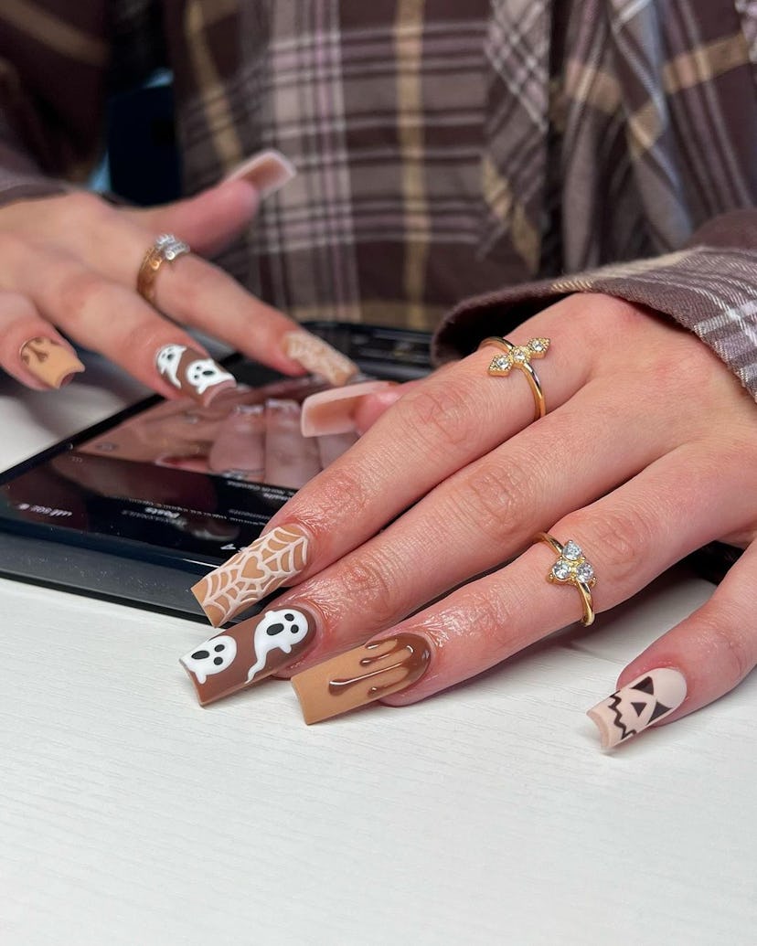 The cutest Halloween nails for 2023 are these chocolate brown ghosts, spiderwebs, and pumpkins.