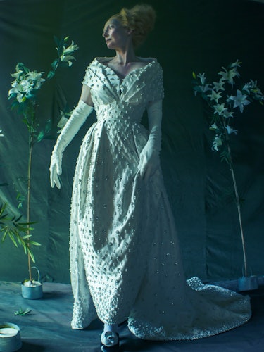 Tilda Swinton wears a white beaded gown and long white gloves.