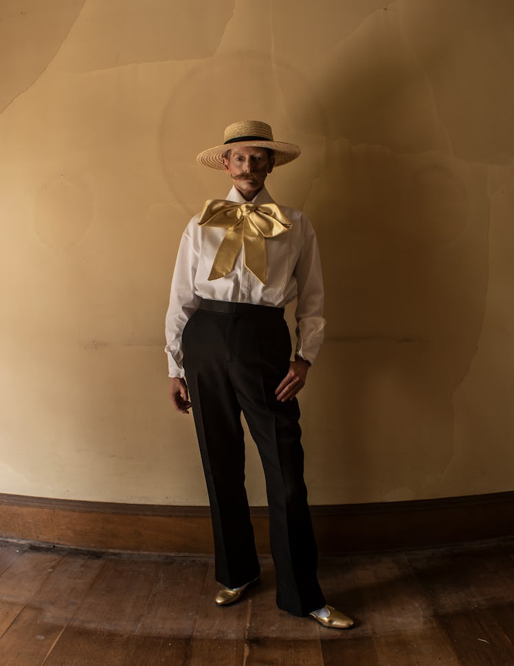 Tilda Swinton wears a white button down shirt, black pants, gold shoes and straw hat.