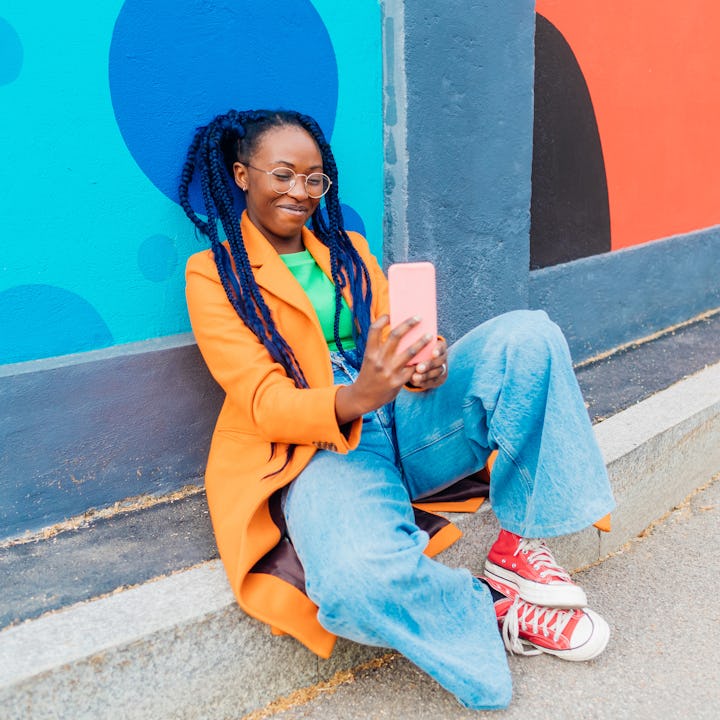 A woman smiles as she takes a selfie while wearing wide legged jeans.