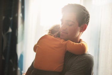 Man holding sleeping daughter as sunlight streams in from window