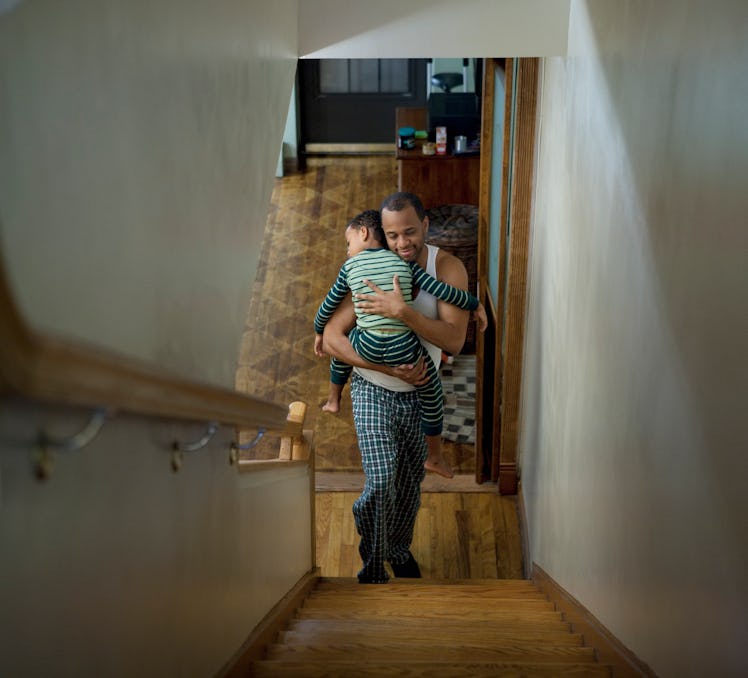 A dad carries his sleeping child up the stairs.