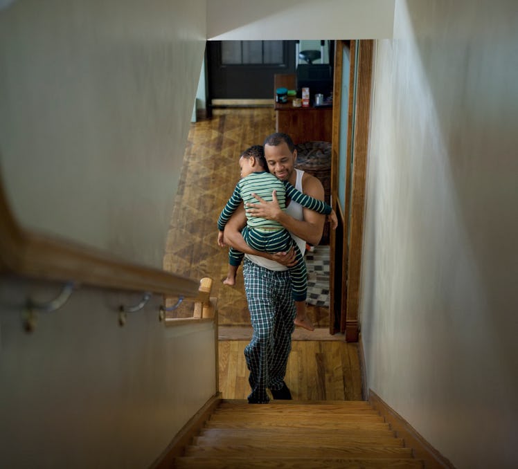 A dad carries his sleeping child up the stairs.