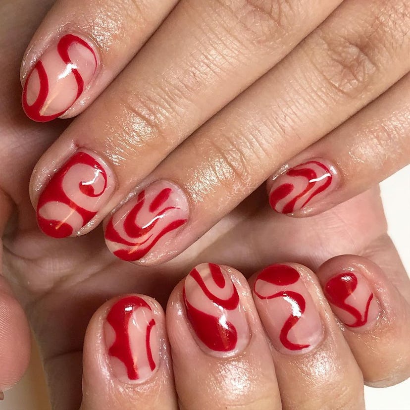 An abstract red swirl nail art design that nods to Taylor Swift’s signature red lipstick.