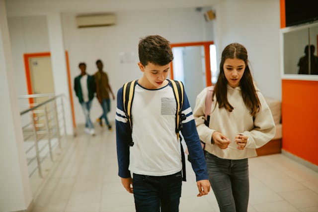 A young teen couple walks together in the hall at school.