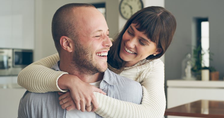 Happy woman hugging her smiling husband from behind in their home