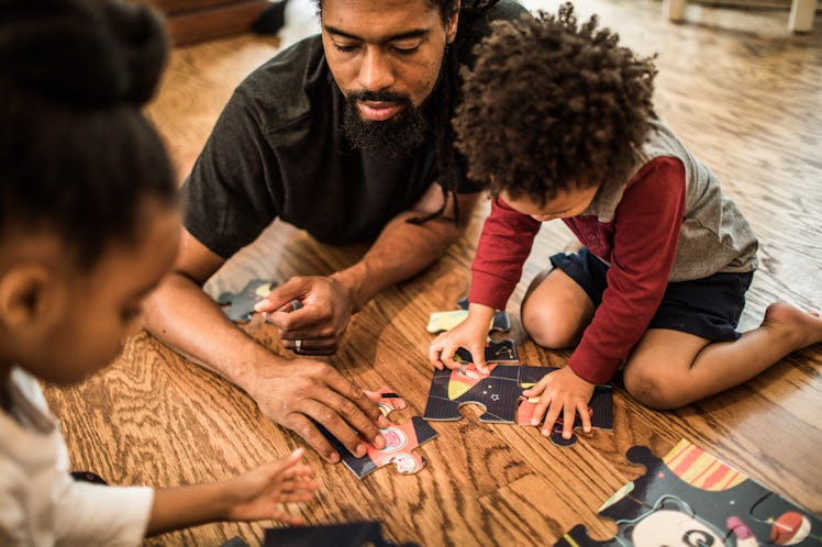 A dad helps his two children do a puzzle on the floor.