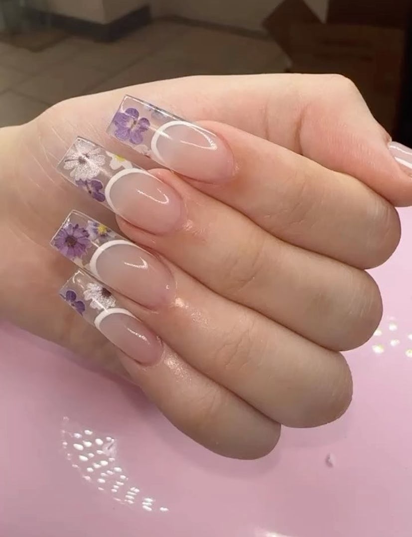 Clear nails with purple and white pressed flowers on square-shaped tips.