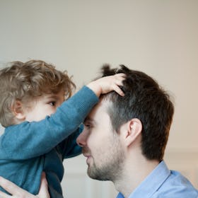 A dad holds his son in the air, as the boy plays with his hair.