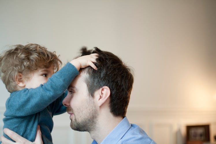 A dad holds his son in the air, as the boy plays with his hair.